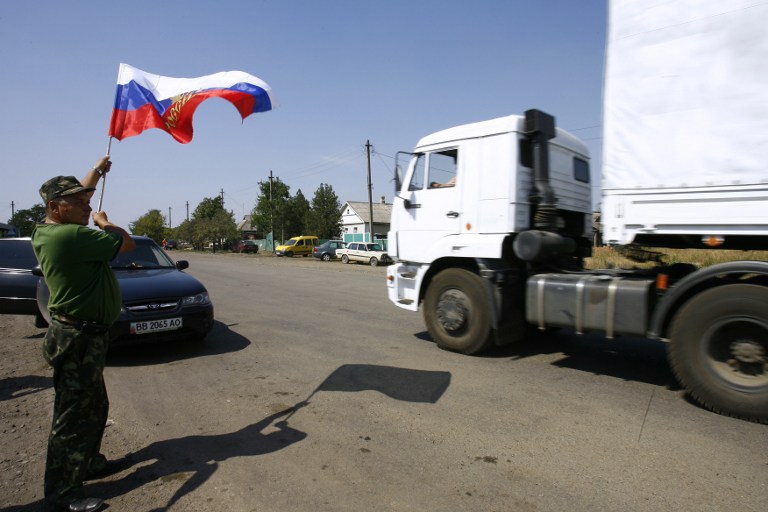 Ucraniano separatista recebe caminhões de ajuda humanitária segurando bandeira da Rússia