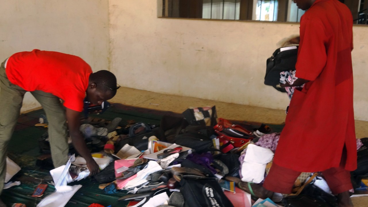Estudante e funcionário de centro de ensino em Kano, na Nigéria, verificam objetos pessoais abandonados por alunos durante ataque