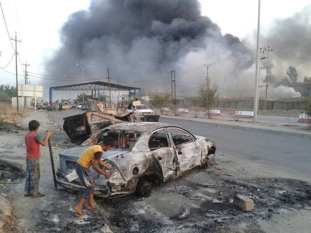 Crianças observam carro destruído após ofensiva dos terroristas do EIIL em Mosul, no Iraque