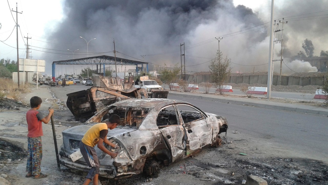 Crianças observam carro destruído após ofensiva terrorista em Mosul, no Iraque