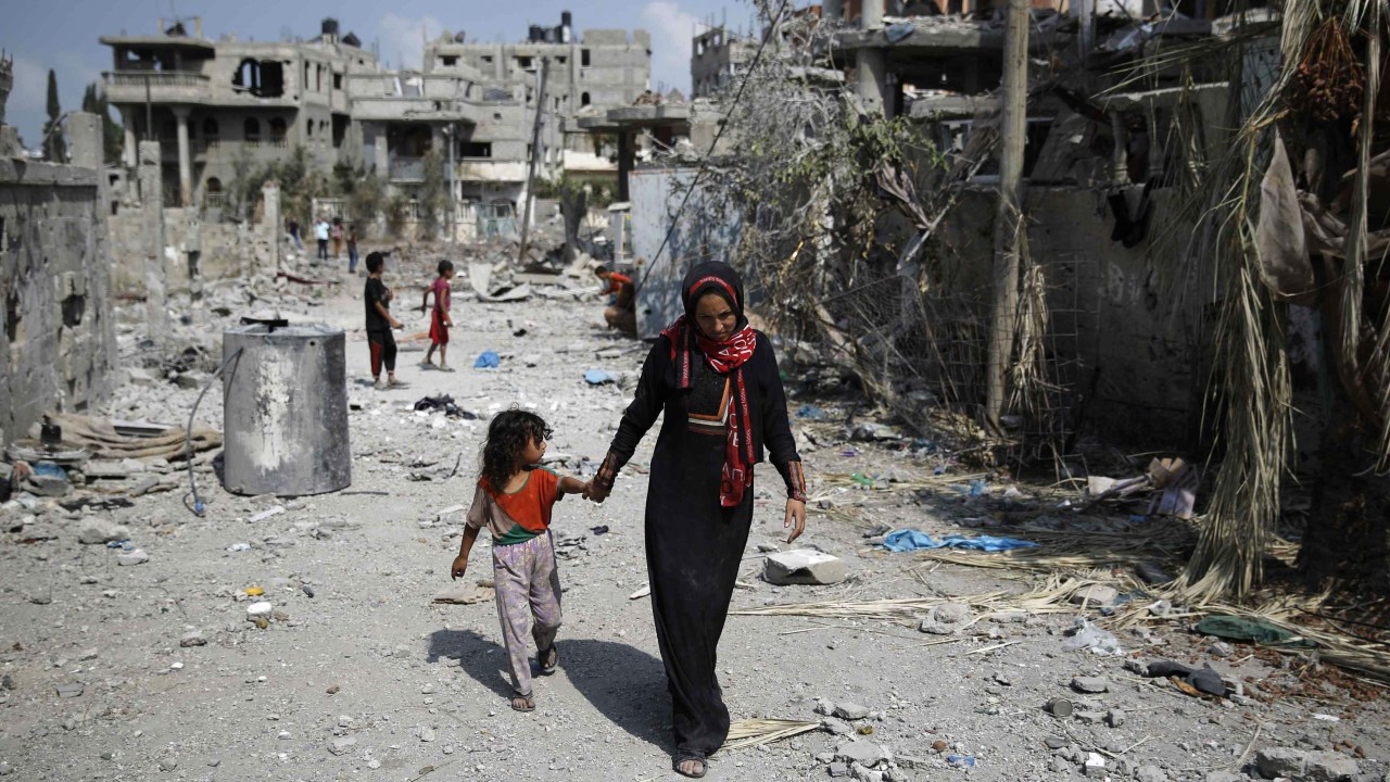 Mulher caminha com a filha pela Faixa de Gaza, após trégua acordada entre Israel e o Hamas
