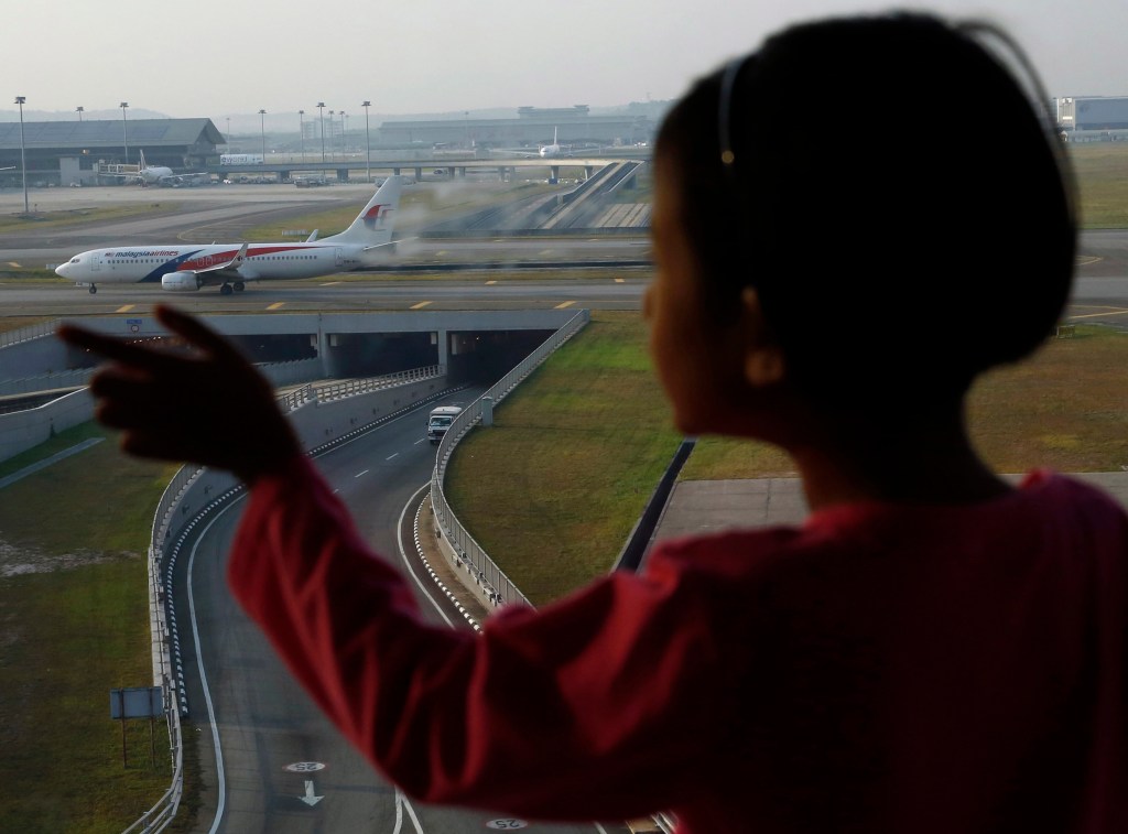 Menina observa avião da Malaysia Airlines no aeroporto internacional de Kuala Lumpur