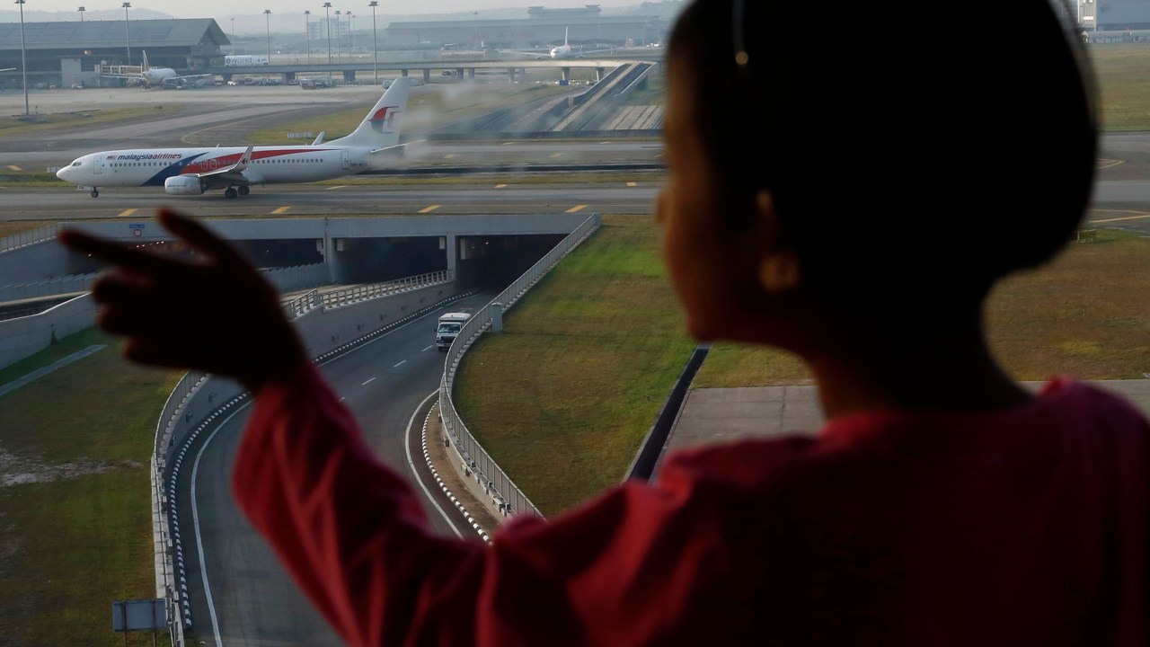 Menina observa avião da Malaysia Airlines no aeroporto internacional de Kuala Lumpur