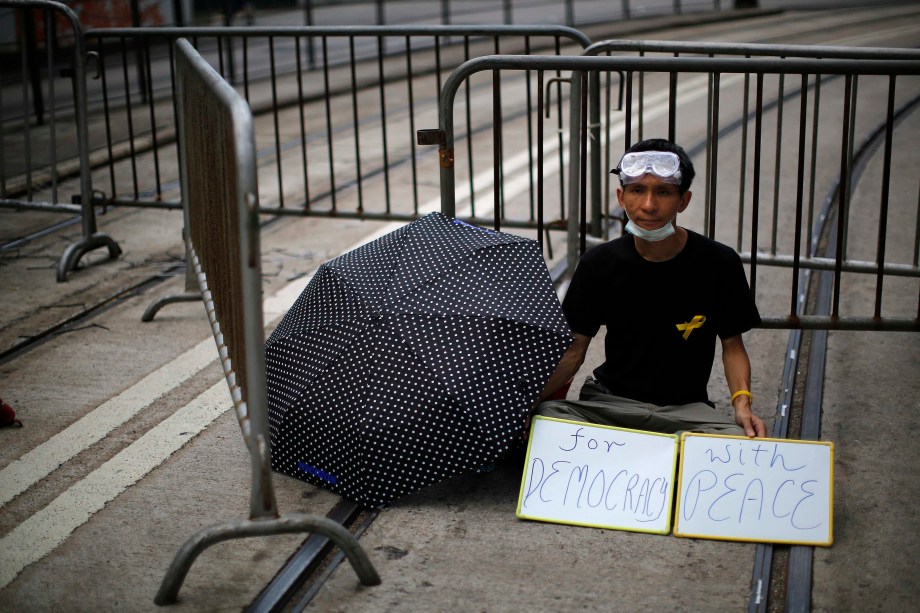 Homem segura cartazes formando a frase “pela democracia, com paz” durante protesto perto de prédios públicos em Hong Kong