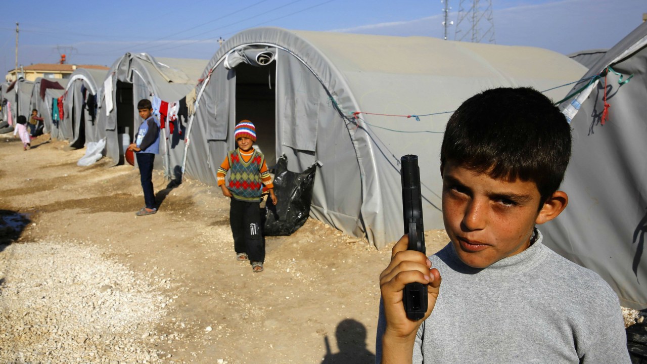 Criança curda segura pistola de brinquedo em campo de refugiados na fronteira entre Síria e Turquia