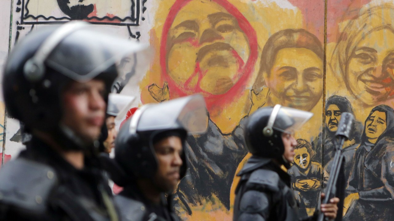 Policiais marcham em frente a mural que lembra vítimas da repressão egípcia no Cairo