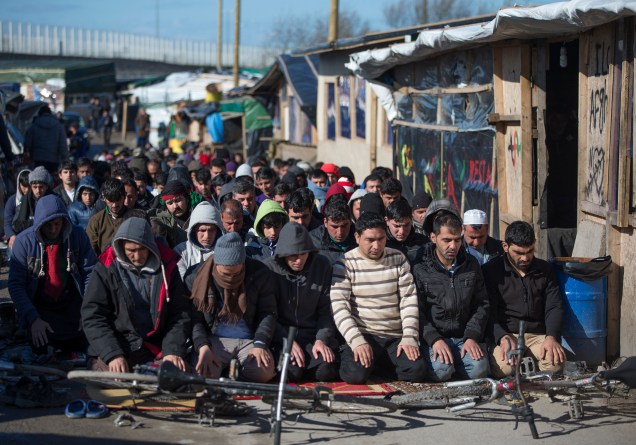 Imigrantes muçulmanos rezam ao lado de acampamento em meio a operação de descupação, em Calais, França. Há anos eles tentam entrar no Reino Unido ilegalmente