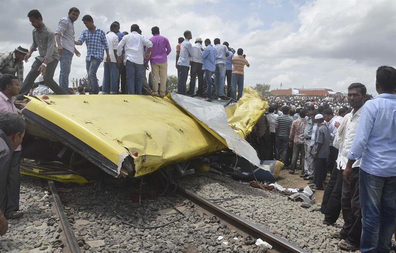 Curiosos próximos aos restos do ônibus escolar que foi atingido por um trem, na Índia