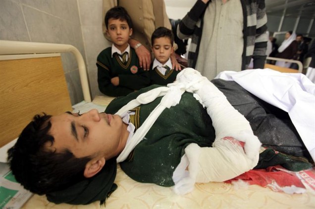 Crianças observam garoto ferido em atentado contra escola no Paquistão