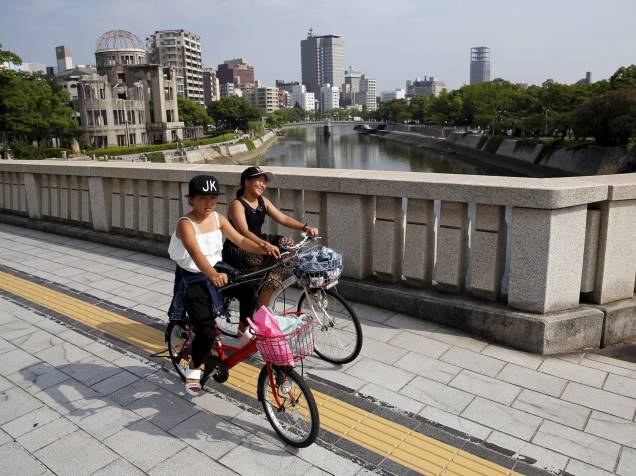 Crianças andam de bicicleta na ponte Aioi, com o Domo da Bomba Atômica ao fundo, em Hiroshima, Japão. No dia 6 de agosto de 1945, os Estados Unidos soltaram a bomba atômica na cidade, matando cerca de 140 mil dos 350 mil residentes de Hiroshima, no primeiro ataque nuclear da história. Três dias depois, uma segunda bomba foi jogada em Nagasaki
