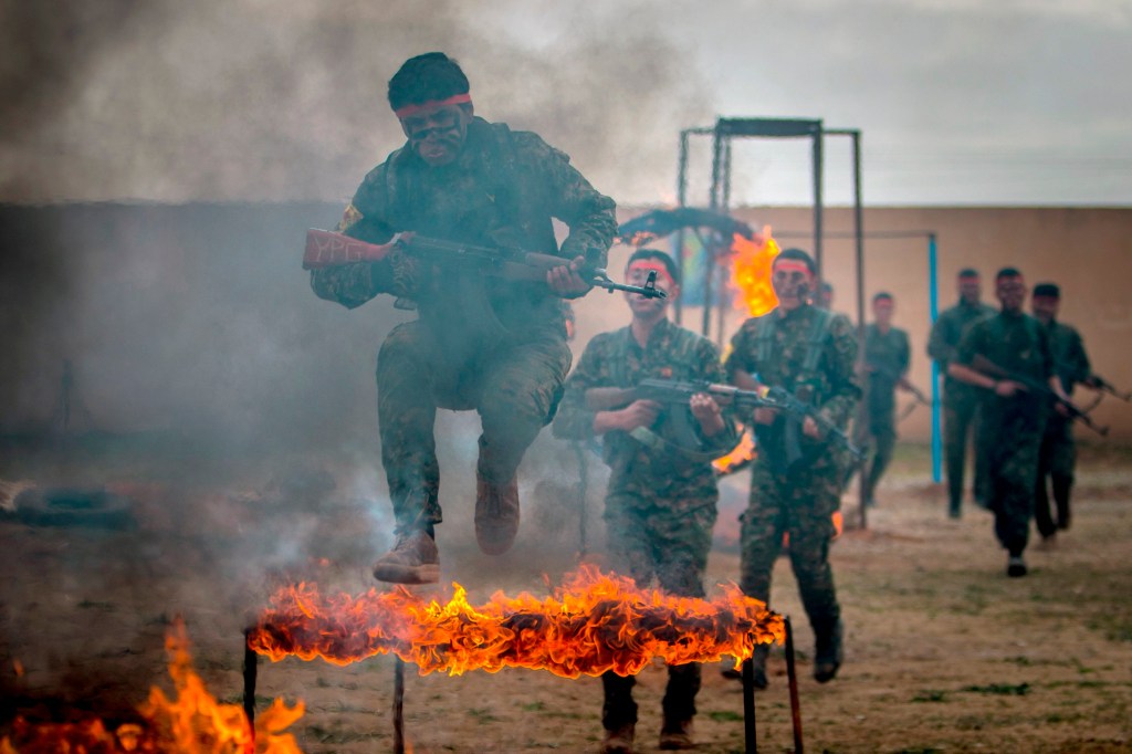 Combatentes curdos das Unidades de Proteção do Povo pulam sobre obstáculo de fogo em campo de treinamento militar