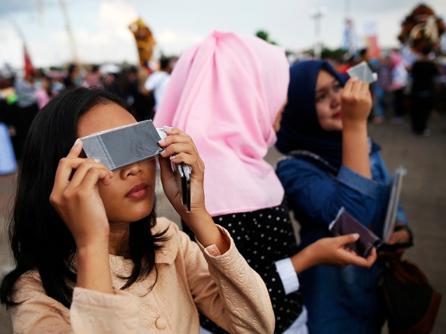 <p>Jovens usam óculos para acompanhar o eclipse total do Sol perto da ponte Ampera ao longo das margens do rio Musi em Palembang, na província de Sumatra do Sul, Indonésia</p>
