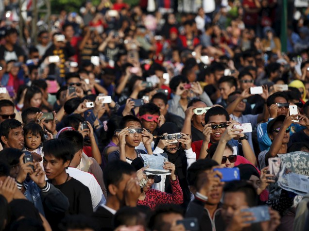 <p>Pessoas usam óculos para acompanhar o eclipse total do Sol perto da ponte Ampera ao longo das margens do rio Musi em Palembang, na província de Sumatra do Sul, Indonésia</p>