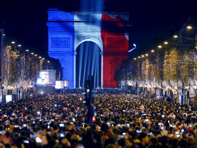 Milhares de pessoas se reúnem perto do Arco do Triunfo, iluminado com as cores da bandeira francesa na Avenida Champs Elysees , em Paris, durante as celebrações de Ano Novo