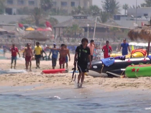Atirador da Tunísia é visto com rifle em mãos enquanto caminha pela praia repleta de turistas
