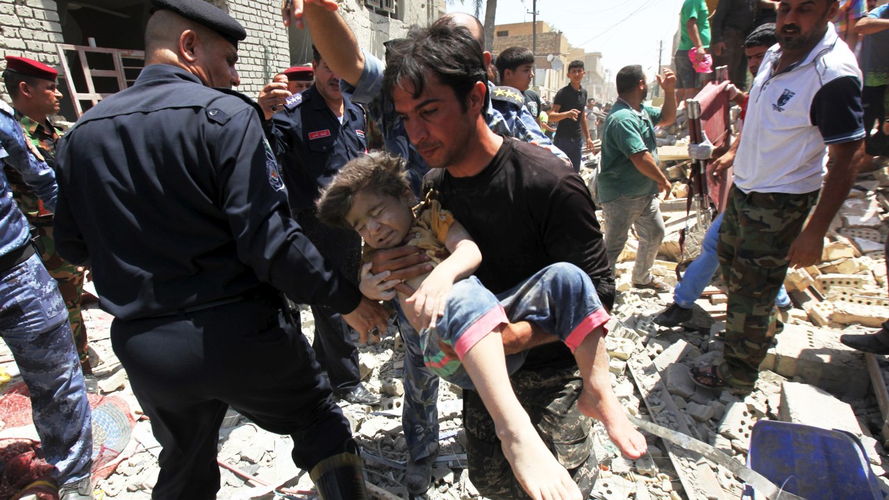 Homem carrega um menino que foi achado debaixo de destroços após bombardeio em Bagdá