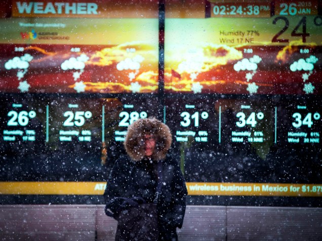 Mulher para debaixo da neve em frente à tela eletrônica com a previsão do tempo na Times Square, em Nova York