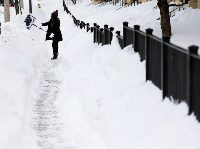 Mulher ajuda a retirar neve acumulada em calçada próxima a escola infantil na Avenida Humbolt, em Boston