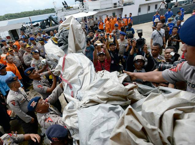 Policiais transportam os restos de um barco que se acredita ser um escorregador de emergência do AirAsia QZ8501, no porto de Kumai, no mar de Java