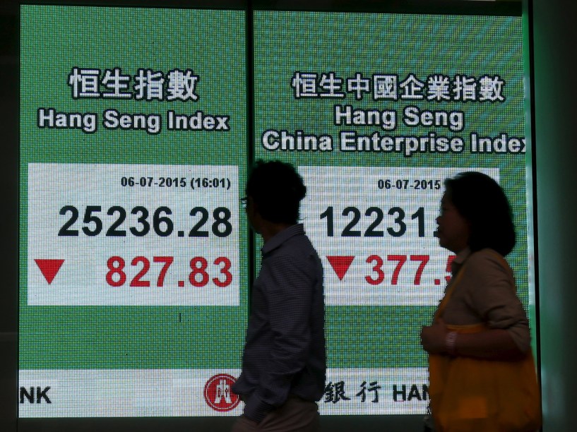 Pessoas passam em frente a um painel com o fechamento da bolsa em Hong Kong, China. O mercado fechou em queda devido ao receio dos investidores de que a crise da Grécia venha a piorar