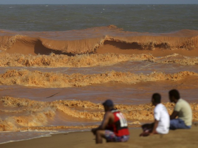 Homens observam o Rio Doce repleto de lama com rejeitos vindos da barragem de Mariana (MG), enquanto o rio se encontra com o mar em Espírito Santo