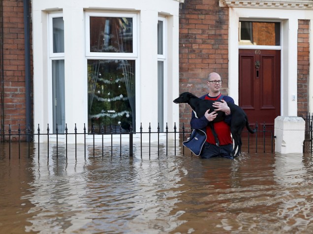Morador local segura seu cão durante tentativa de atravessar uma rua inundada em Carlisle, Grã-Bretanha