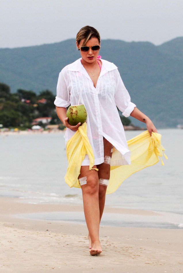 Andressa Urach caminha em uma praia de Florianópolis com curativos nas pernas