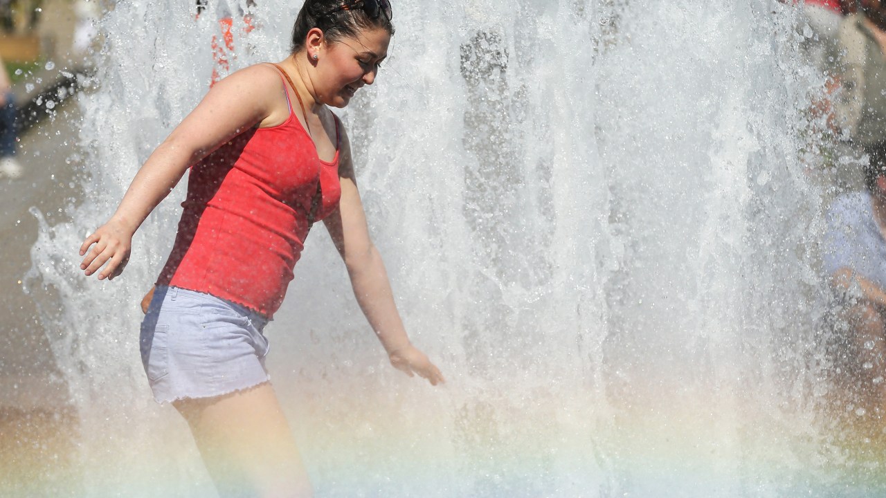 Mulher se refresca em uma fonte pública, enquanto o spray de água cria um arco-íris no centro de Berlim, na Alemanha - 02/07/2015