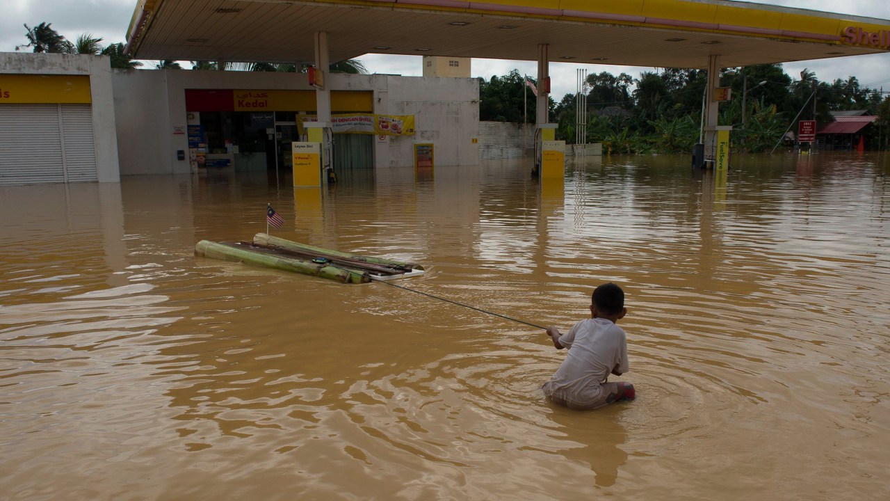 Menino brinca próximo a um posto de gasolina coberto por água em Kota Bharu, na Malásia. O país enfrenta uma grave enchente que obrigou mais de 100 mil pessoas a deixarem suas casas