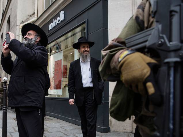 Judeus observam a circulação de policiais frances que reforçam a segurança no bairro de Marais, em Paris