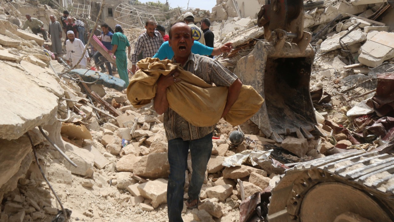 Homem carrega corpo que foi removido dos escombros de um prédio após um explosão causada por forças do governo, em Aleppo, Síria