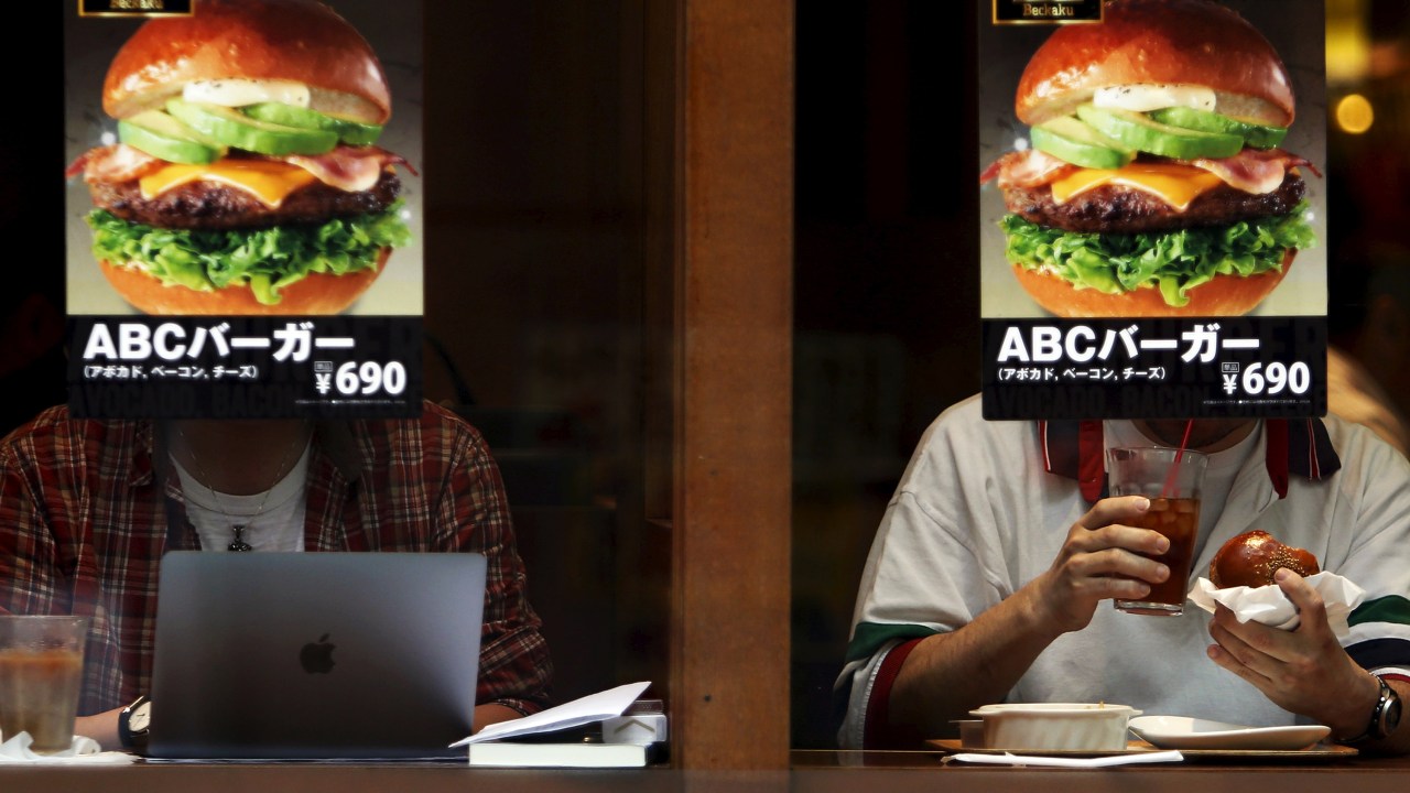 Clientes são fotografados por trás de uma propaganda de hamburger em uma lanchonete fast food no distrito Akihabara, em Tóquio no Japão