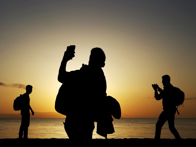 Imigrantes com destino à Grécia, fotografam o pôr-do-sol após desembarcarem na ilha grega de Kos