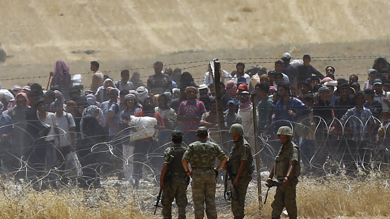Soldados turcos observam enquanto refugiados sírios aguardam atrás das cercas para atravessar a fronteira entre Turquia e Síria - 05/06/2015