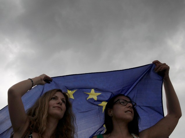 Manifestantes se protegem da chuva com uma bandeira da União Europeia durante protesto em apoio à permanência do país na zona do euro, em frente ao parlamento em Atenas, Grécia - 30/06/2015
