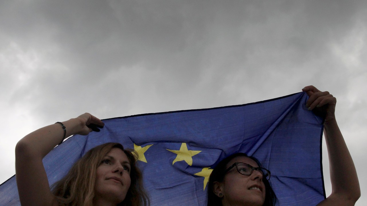 Manifestantes se protegem da chuva com uma bandeira da União Europeia durante protesto em apoio à permanência do país na zona do euro