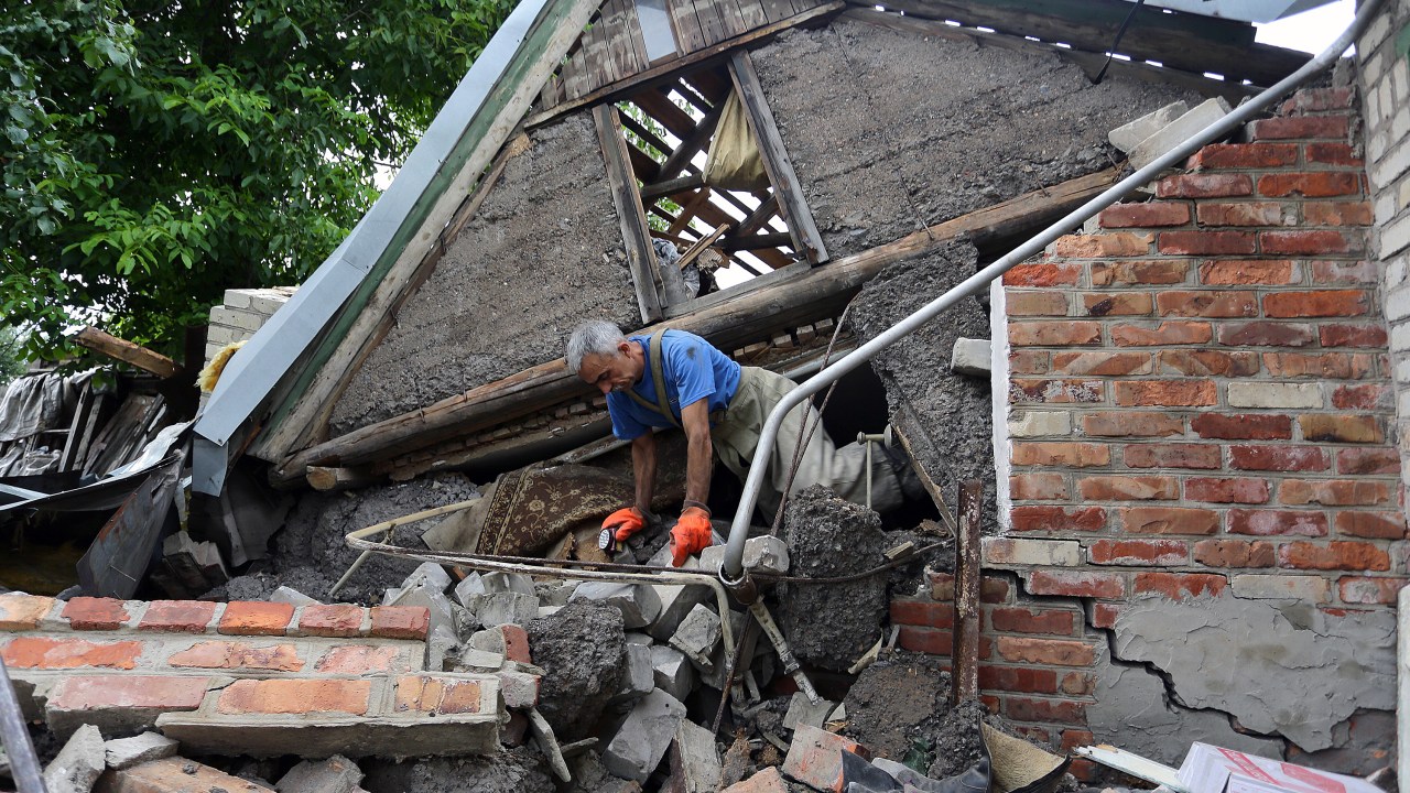 Homem trabalha no resgate do corpo de uma mulher presa debaixo dos escombros de sua casa na vila de Golmovsky, na região de Donetsk, após confronto entre forças ucranianas e separatistas pró-russos - 28/07/2015