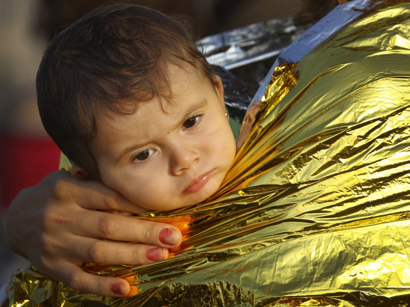 Criança refugiada síria é carregada no colo enrolada em um cobertor térmico no porto de Kos, após uma missão de resgate na ilha grega. Guarda Costeira italiana resgatou 60 refugiados sírios à deriva em um bote entre a Grécia e a Túrquia