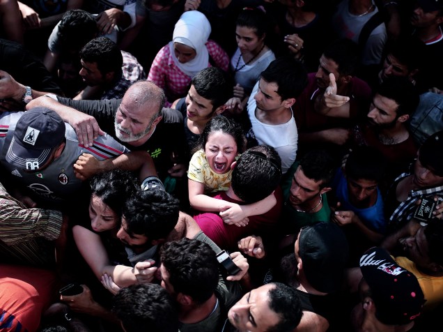 Criança chora em meio a uma multidão de imigrantes, durante um procedimento de registro em um estádio, na ilha grega de Kos