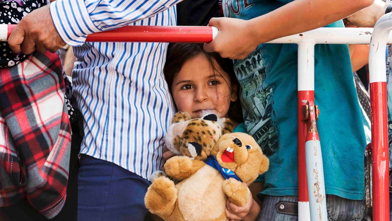 Menina refugiada leva seu urso de pelúcia enquanto tenta entrar em Munique, na Alemanha com sua família