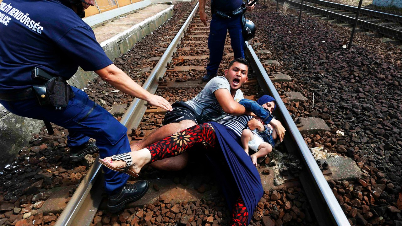 Família de refugiados se protege de policiais na estação ferroviária na cidade de Bicske, Hungria. A composição seguia para a fronteira com a Áustria.
