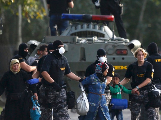Policiais levam mulher e criança migrantes durante confronto em Roszke, na Hungria, nesta quarta-feira (16)
