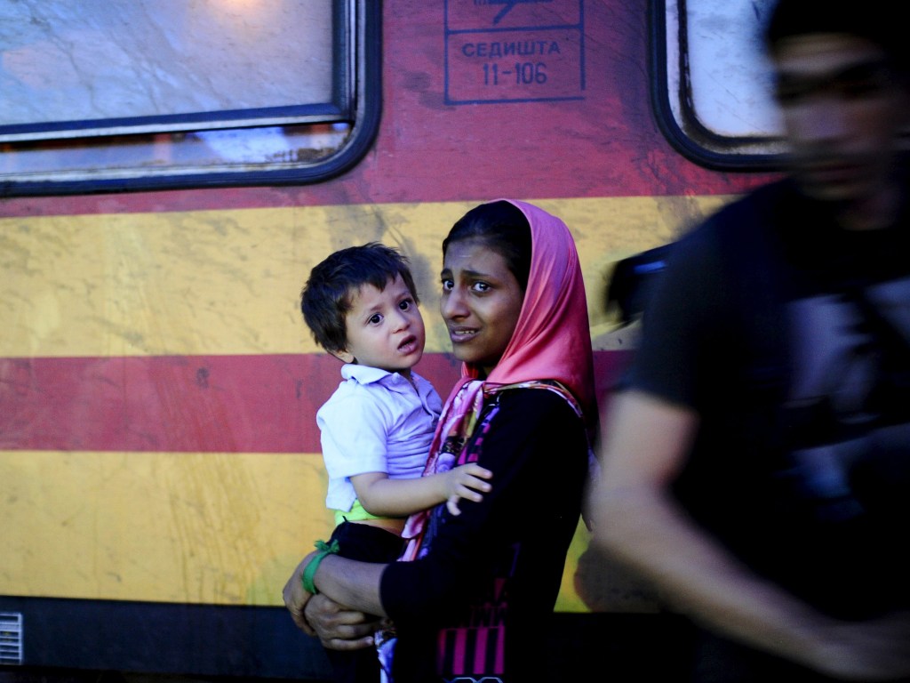 Mulher carrega seu filho entre um grupo de refugiados que tentam embarcar em um trem no campo de trânsito de Gevgelija, na Macedônia - 23/09/2015