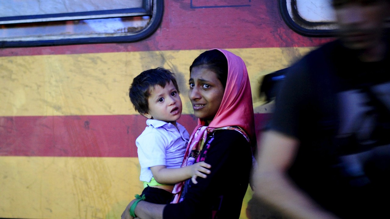 Mulher carrega seu filho entre um grupo de refugiados que tentam embarcar em um trem no campo de trânsito de Gevgelija, na Macedônia - 23/09/2015