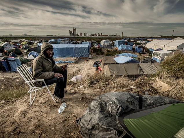 Homem usa um celular para ligar para sua família no Sudão. Ele vive no acampamento criado para imigrantes africanos em Calais, na França