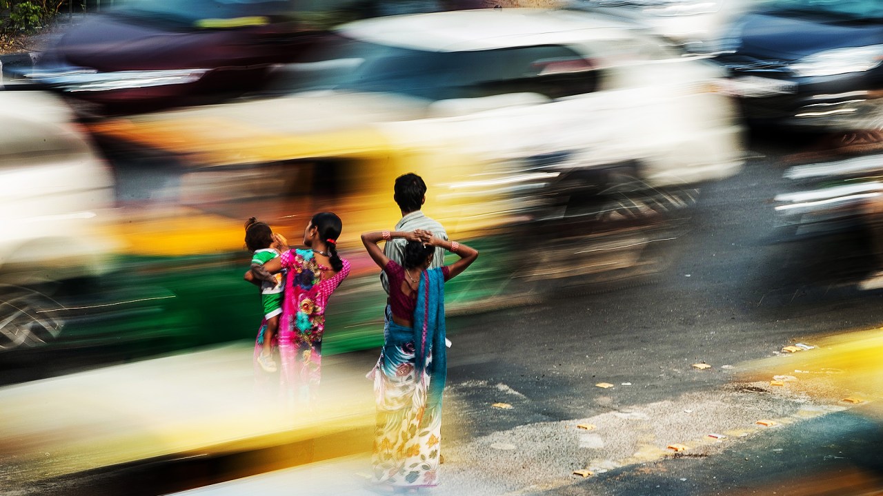 Pedestres aguardam em um ponto de ônibus sem proteção localizado em calçada no meio de faixas de carro em Nova Délhi, na Índia, durante a hora do rush