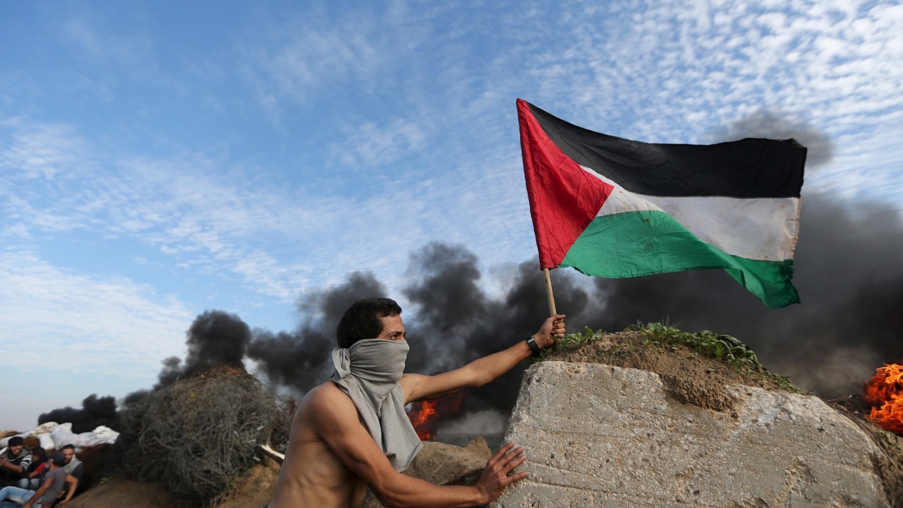 Manifestante carrega uma bandeira palestina durante confronto com tropas israelenses na fronteira entre Israel e a Faixa de Gaza - 20/11/2015