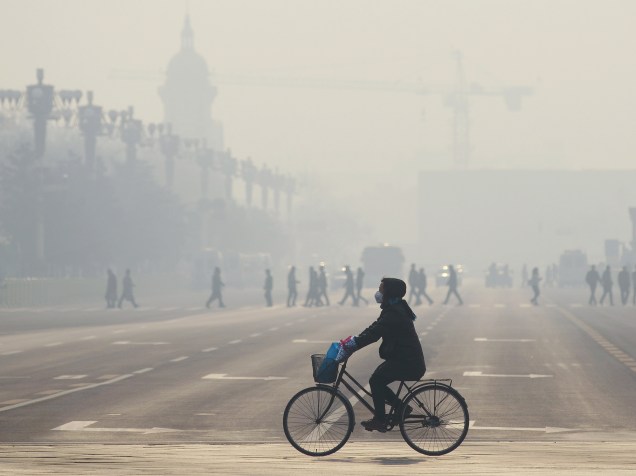 <p>Mulher usa máscara enquanto anda de bicicleta ao longo de uma rua, perto da praça de Tiananmen. Pequim está em "alerta vermelho" para a poluição do ar</p>