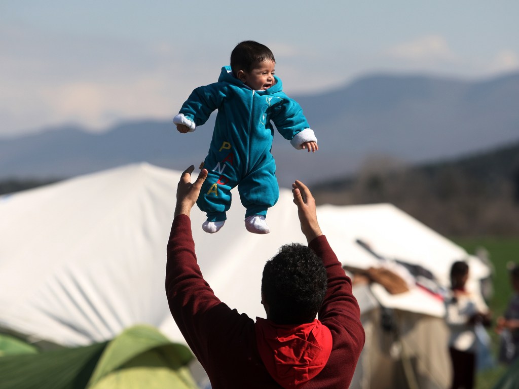 Refugiado brinca com seu filho na fronteira entre Grécia e Macedônia, na quinta-feira (25), após as restrições de passagem adicionais impostas pelas autoridades macedônias que deixaram centenas de presos perto da aldeia de Idomeni, na Grécia