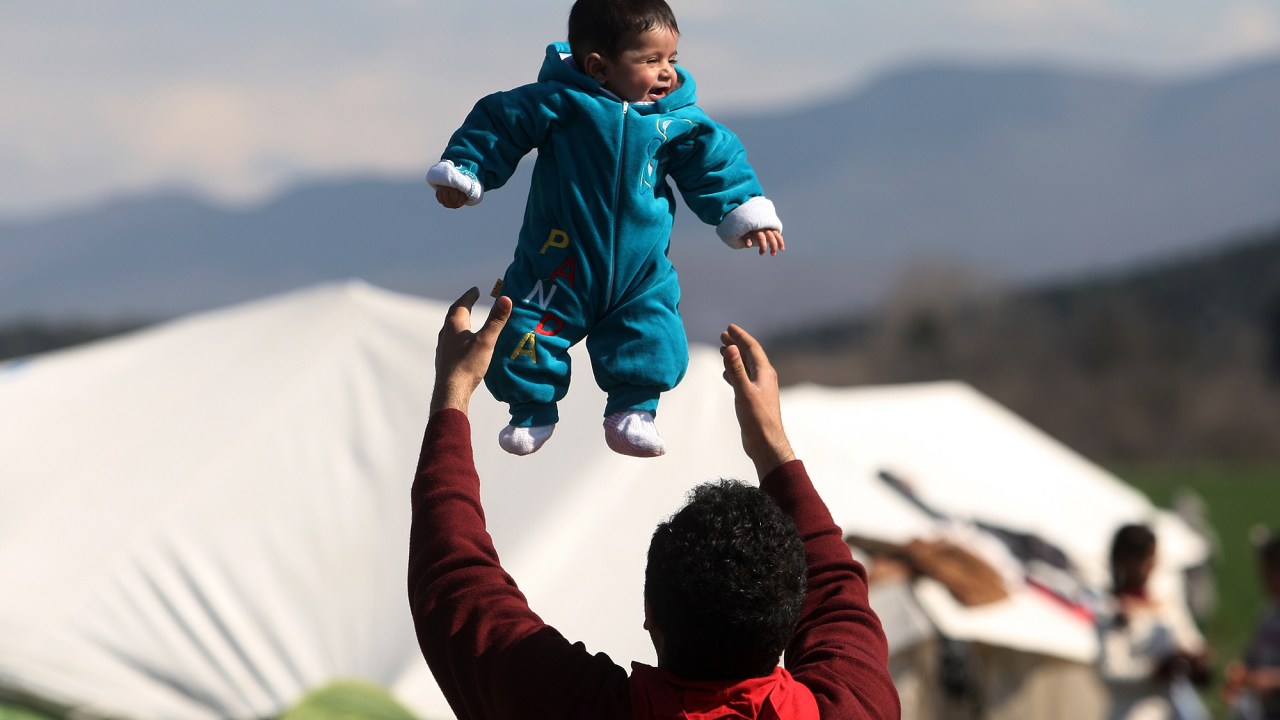 Refugiado brinca com seu filho na fronteira entre Grécia e Macedônia, na quinta-feira (25), após as restrições de passagem adicionais impostas pelas autoridades macedônias que deixaram centenas de presos perto da aldeia de Idomeni, na Grécia
